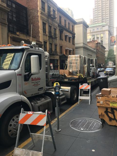 A flatbed truck on a busy San Francisco street delivering a load and our forklift to move the load inside